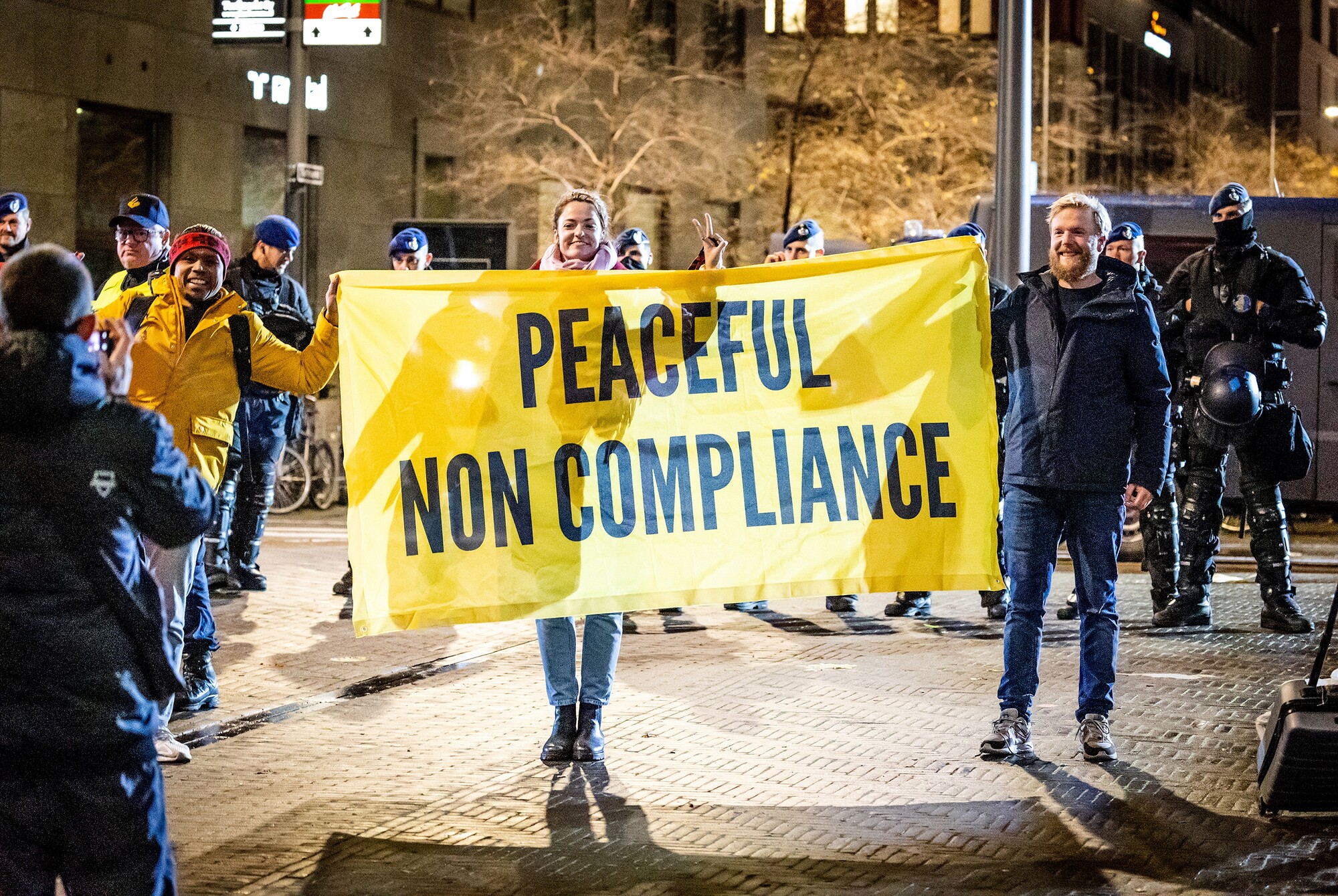 Mensen protesteren 's avonds op straat met een spandoek. Een noodverordering geldt voor de binnenstaad van Den Haag tijdens de corona persconferentie. 